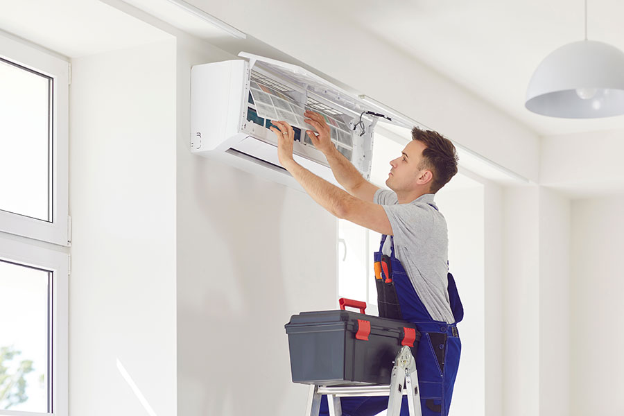 Certified HVAC technician inserting clean washable filtration panel into ductless mini-split wall cabinet